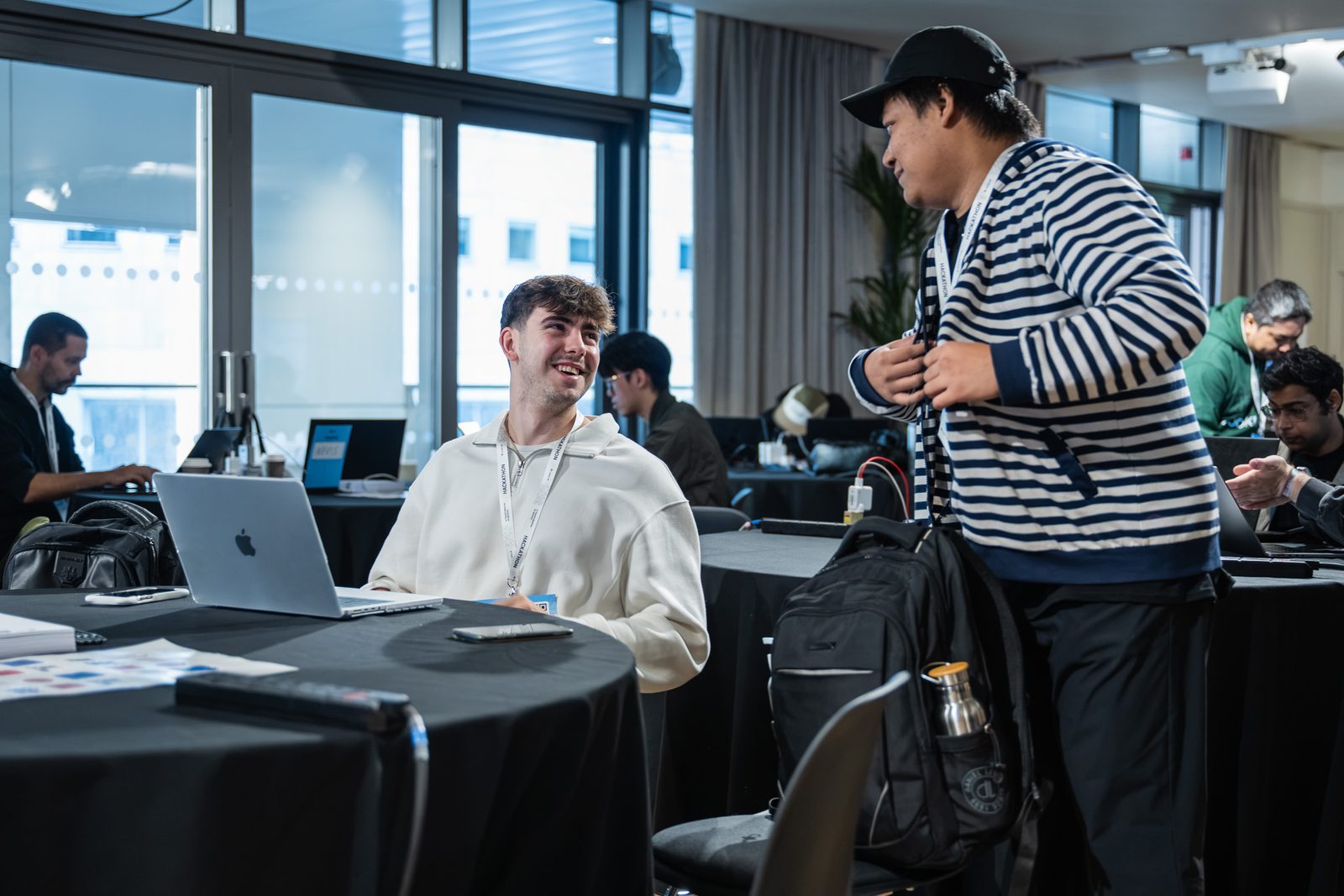 Two teammates chatting at a table of laptops during the hackathon